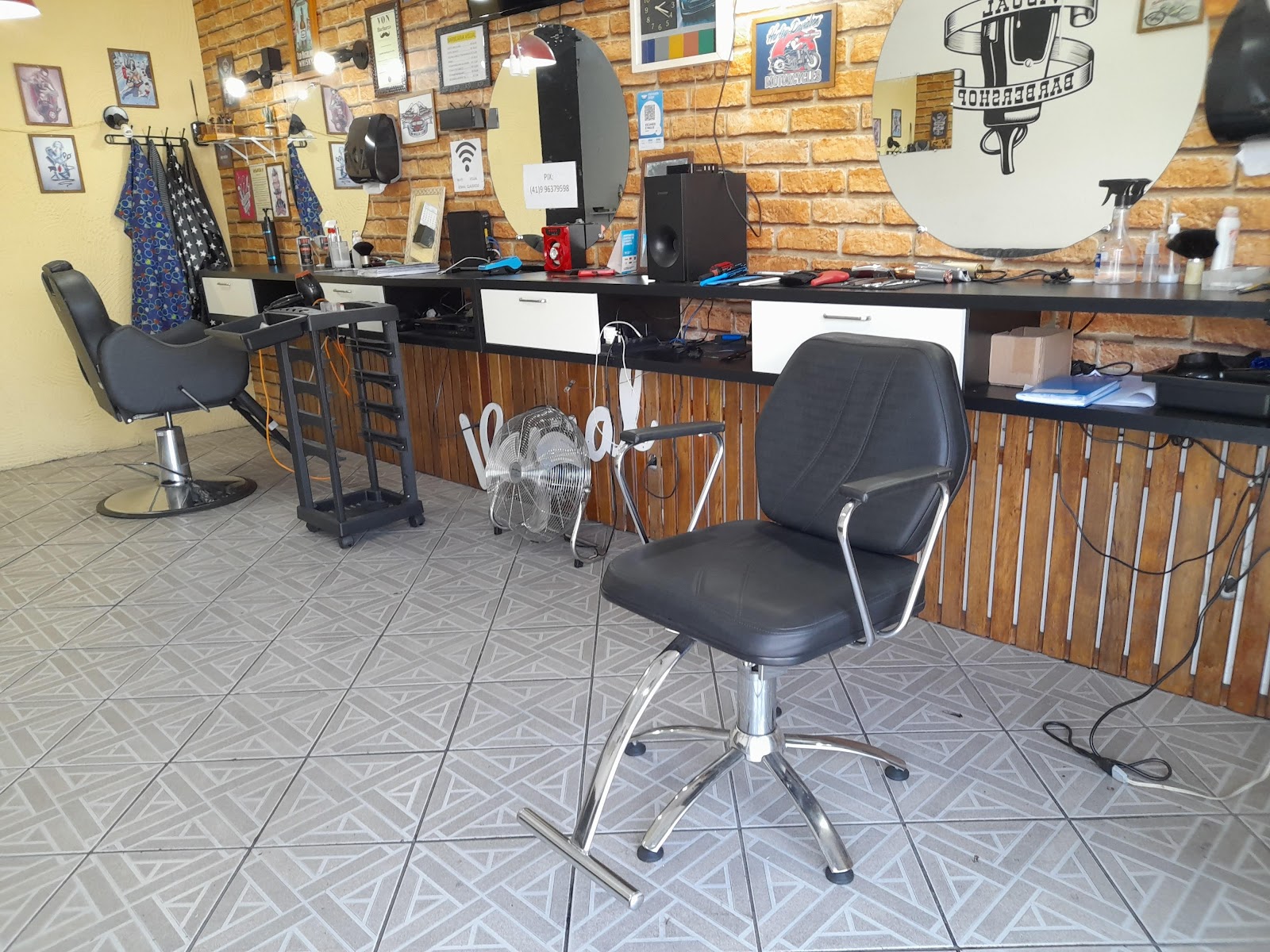 Estação de trabalho da Barbearia Visual, com espelhos redondos e parede de tijolo aparente