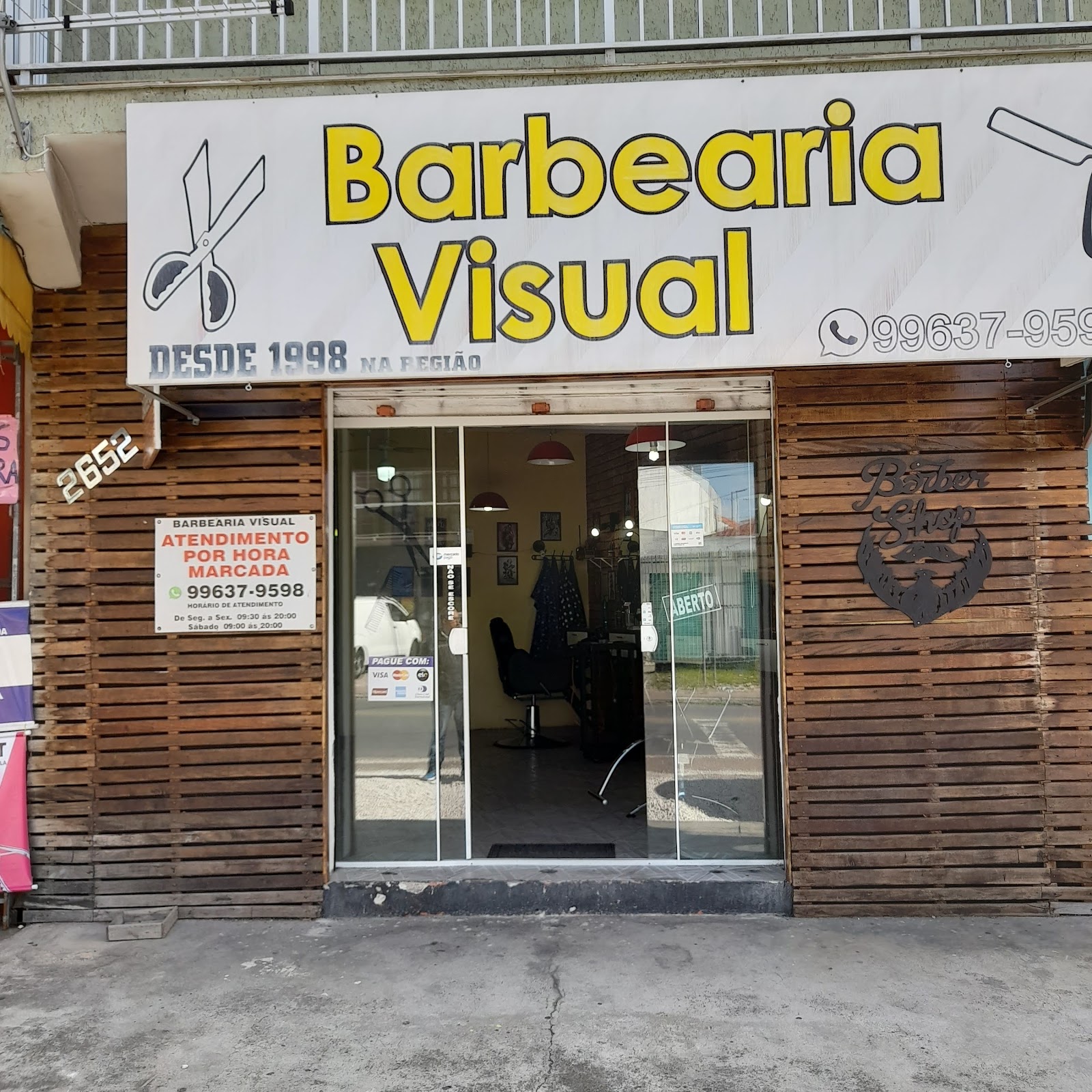 Fachada da Barbearia Visual, com letreiro amarelo e a inscrição Desde 1998 na região
