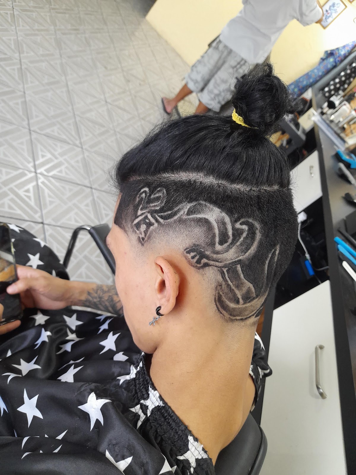 Desenho de dragão raspado na lateral da cabeça de um cliente, com coque no topo