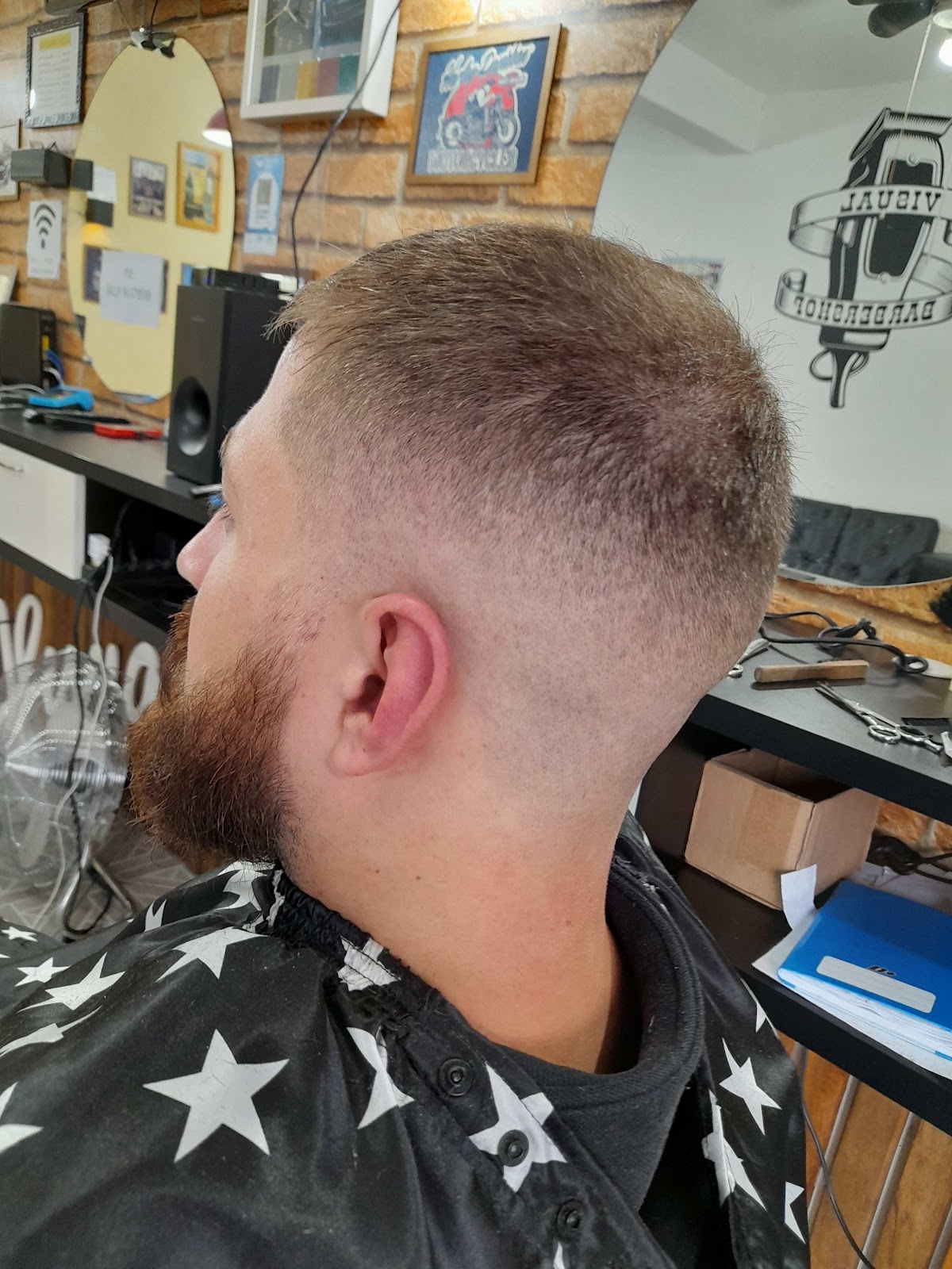 Corte degradê visto de perfil, com o logo Visual Barbershop refletido no espelho